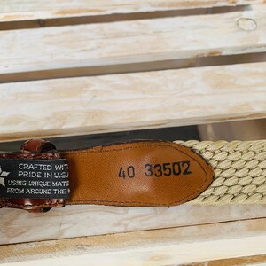 Puede incluir: Primer plano de un cintur&oacute;n tejido marr&oacute;n y beige. El cintur&oacute;n tiene una etiqueta de cuero con el n&uacute;mero "40 33502" en relieve. El cintur&oacute;n est&aacute; fabricado con orgullo en los EE. UU.
