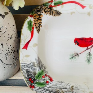 May include: White ceramic serving dish with a gold rim. The dish features a festive Christmas design with red cardinals, pine branches, holly berries, pine cones, and red ribbon.