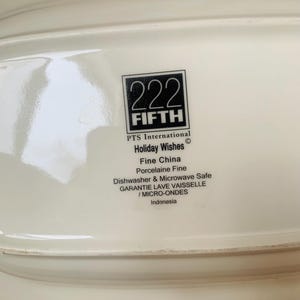 May include: White ceramic serving dish with a black and white logo that reads "222 FIFTH PTS International Holiday Wishes Fine China Porcelaine Fine Dishwasher & Microwave Safe GARANTIE LAVE VAISSELLE / MICRO-ONDES Indonesia"