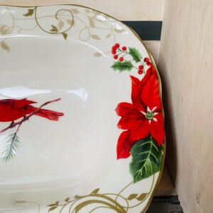May include: White oval serving dish with a gold rim and a Christmas design. The design features a red cardinal bird, red poinsettia flowers, and green leaves.