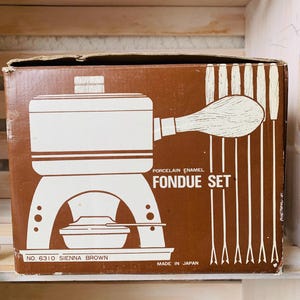May include: A vintage brown box with a white graphic of a fondue set. The box reads "Porcelain Enamel Fondue Set" and "No. 6310 Sienna Brown". The set includes a pot, burner, and forks. Made in Japan.