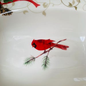 May include: White ceramic serving dish with a red cardinal perched on a pine branch. The dish has a gold and green floral design around the rim.