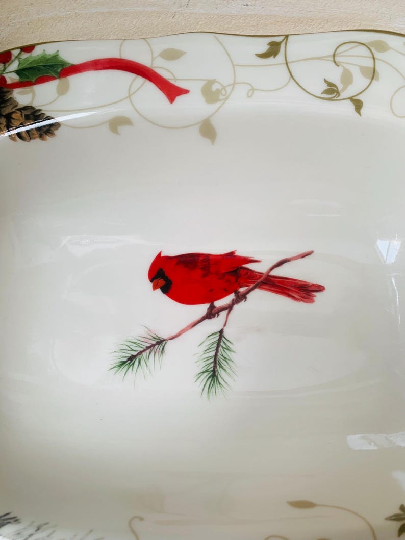 May include: White ceramic serving dish with a red cardinal perched on a pine branch. The dish has a gold and green floral design around the rim.