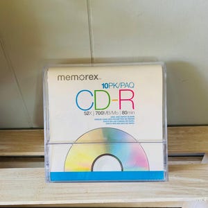 May include: A Memorex 10-pack of CD-R discs in a clear plastic case. The white insert features the text 10PK/PAQ, CD-R, 52X, 700MB/Mo, and 80min. A graphic of a circular disc with a rainbow iridescent finish is printed at the bottom of the insert.