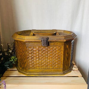 Peut inclure: Un coffre de rangement en bois vintage avec un panneau avant tissé et un couvercle à charnière. La boîte est de forme octogonale et comporte un loquet marron foncé. La boîte est posée sur une palette en bois.
