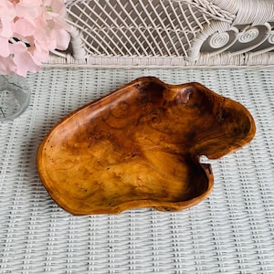 May include: A handcrafted wooden bowl with a natural, organic shape. The bowl is made of a warm, reddish-brown wood with visible grain patterns. The bowl's unique shape and color make it a decorative piece for the home.