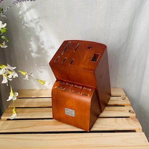May include: A wooden knife block with multiple slots for various knives. The block is a warm brown color and has the "Chicago Cutlery" logo on the front. It is sitting on a wooden pallet.