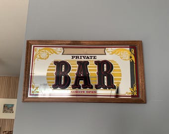 Pode incluir: Um espelho de parede retangular com moldura de madeira e um design decorativo. O espelho exibe o texto PRIVATE BAR em letras grandes pretas com contornos vermelhos, e as palavras ALWAYS OPEN em texto vermelho menor abaixo do título.