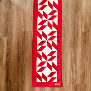 May include: A rectangular red and white quilt with a star pattern. The quilt is made of red fabric with white star-shaped designs. The quilt is approximately 12 inches wide and 30 inches long.