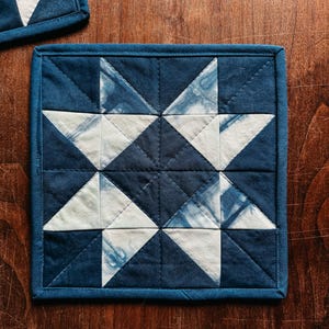 以下が含まれることがあります： 星型のデザインが施された、正方形のキルトコースター。コースターは、ネイビーブルーと白の配色です。デザインは三角形と正方形で構成されています。コースターのサイズは約15cm&times;15cmです。