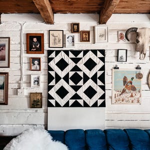 May include: A living room with a blue velvet sofa, white faux fur cushion, and a wall decorated with framed pictures and a black and white geometric quilt. The ceiling has exposed wooden beams.