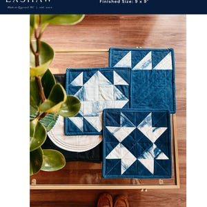 以下が含まれることがあります： インディゴブルーと白のキルト鍋つかみ3点セット。星柄のデザインです。各鍋つかみは22.86 cm x 22.86 cmです。画像には「POTHOLDER TRIO」と「EXSHAW」の文字が含まれています。