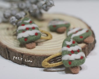 Puede incluir: Horquillas para el pelo con forma de árbol de Navidad de fieltro verde, adornadas con bayas rojas y detalles blancos de nieve. Los árboles están sobre horquillas doradas. Se muestran sobre una rodaja de madera con el texto "Petit Lion".