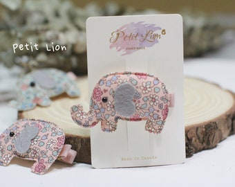 May include: A selection of pink and floral elephant hair clips with grey felt ears and small pink bows. The clips are presented on a white card with the text "Petit Lion" and "Made in Canada".
