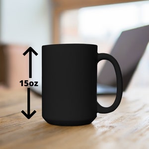 Op de afbeelding: Een zwarte keramische mok met een handvat, 15oz. De mok staat op een houten oppervlak.