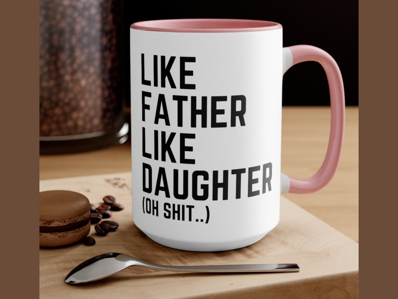 May include: White ceramic coffee mug with a pink rim and handle. The mug has black text that reads "Like Father Like Daughter (Oh Shit..)"