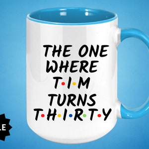 May include: White ceramic mug with a blue rim and handle. The mug features black text that reads "The One Where Tim Turns Thirty" with colorful dots replacing the vowels in the words.