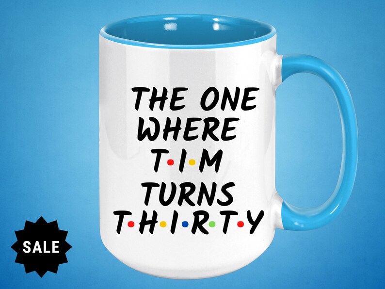 May include: White ceramic mug with a blue rim and handle. The mug features black text that reads "The One Where Tim Turns Thirty" with colorful dots replacing the vowels in the words.