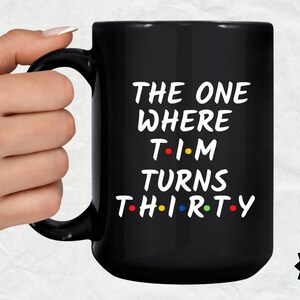 May include: Black coffee mug with white text that reads "The One Where Tim Turns Thirty" with colorful dots replacing the vowels.