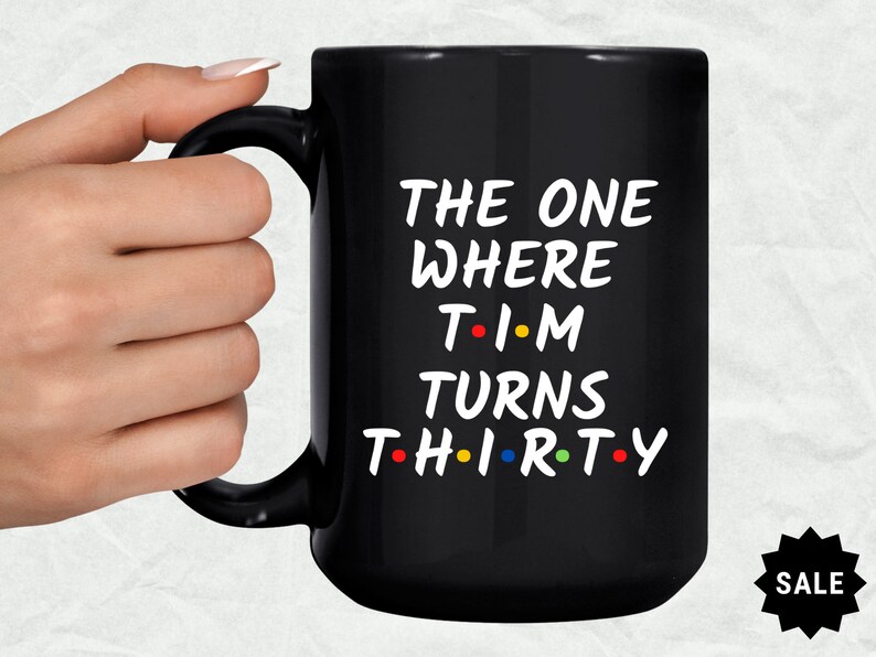 May include: Black coffee mug with white text that reads "The One Where Tim Turns Thirty" with colorful dots replacing the vowels.