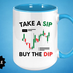May include: White ceramic mug with a blue rim and handle. The mug has a black and green graphic of a stock market chart with the text "TAKE A SIP BUY THE DIP".