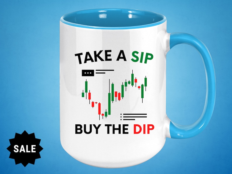 May include: White ceramic mug with a blue rim and handle. The mug has a black and green graphic of a stock market chart with the text "TAKE A SIP BUY THE DIP".