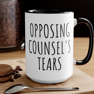 May include: White ceramic coffee mug with a black rim and handle. The mug has black text that reads "Opposing Counsel's Tears".