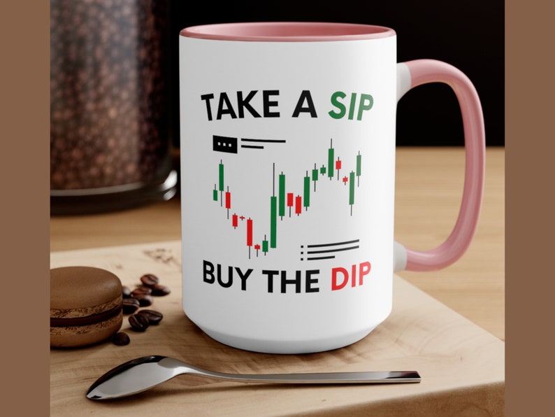 May include: White ceramic mug with a pink rim and handle. The mug has a black and green stock chart graphic and the text "TAKE A SIP BUY THE DIP".
