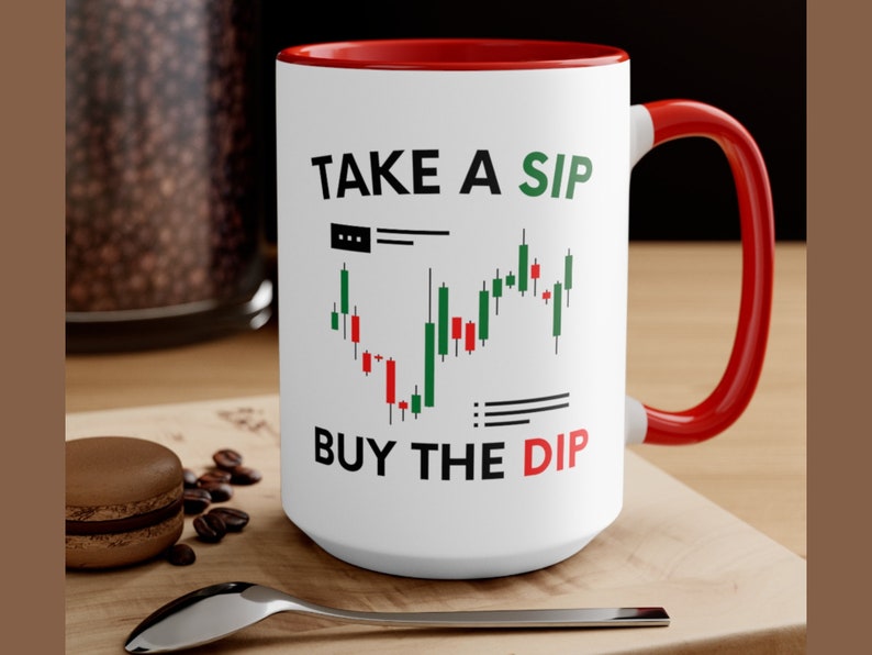May include: White ceramic coffee mug with a red rim and handle. The mug has a black and green stock chart graphic and the text "TAKE A SIP BUY THE DIP".