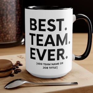 May include: White ceramic coffee mug with a black rim and handle. The mug has black text that reads "BEST. TEAM. EVER." and "(ADD TEAM NAME OR JOB TITLE)".