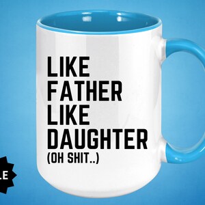 May include: White ceramic coffee mug with a blue rim and handle. The mug has black text that reads "Like Father Like Daughter (Oh Shit...)"