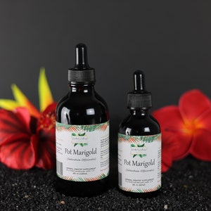 May include: Two bottles of Pot Marigold herbal supplement, one larger and one smaller, with dropper tops. The bottles are dark brown glass with white labels and green accents. The bottles are sitting on a black surface with red and yellow flowers.