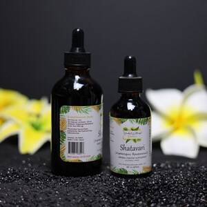May include: Two brown glass bottles with dropper tops, one larger than the other, on a black surface. The smaller bottle has a label that reads "Shatavari" and "Ayurvedic Rejuvenating Herbal Dietary Supplement". The larger bottle has a label with text that is too small to read.