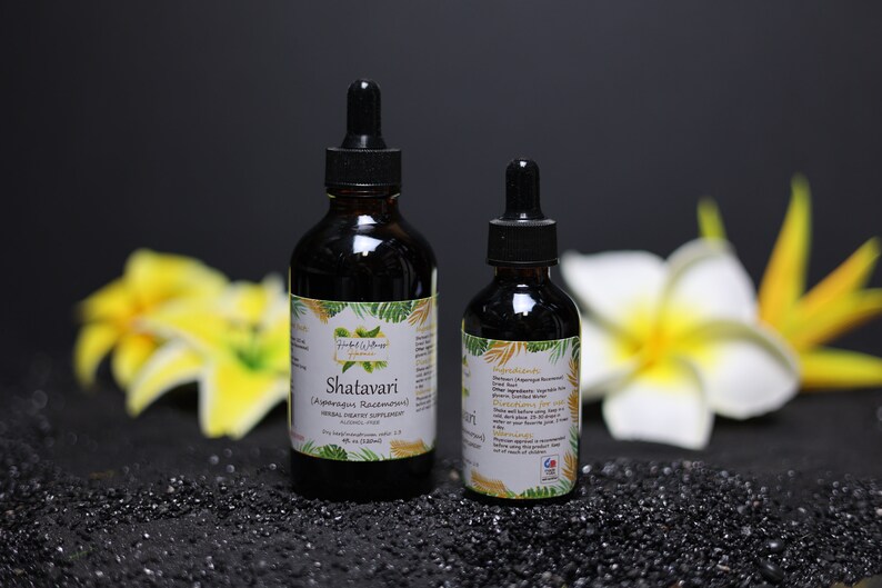 May include: Two bottles of Shatavari (Asparagus Racemosus) herbal extract, one larger and one smaller, with a white label and green foliage design. The bottles are on a black surface with yellow flowers in the background.