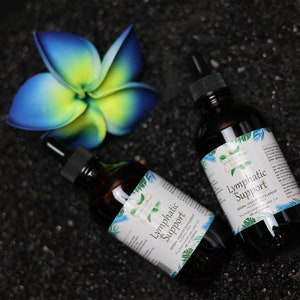 May include: Two brown glass bottles with droppers, labelled "Lymphatic Support" on a black background. The bottles are surrounded by a blue and yellow flower.
