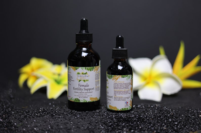 Może przedstawiać: Dwie bursztynowe butelki ze szklanymi kroplomierzami zawierające ciemny płyn. Większa butelka jest oznaczona etykietą "Female Fertility Support Herbal Dietary Supplement", a mniejsza butelka jest oznaczona etykietą "Unflavored". Obie butelki stoją na czarnej powierzchni z ż&oacute;łtymi kwiatami w tle.