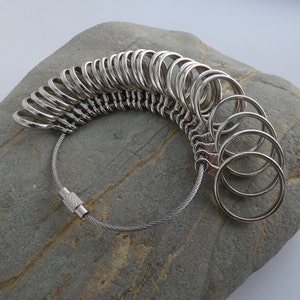 May include: A silver ring sizer with a chain and a clasp. The sizer has a series of rings of different sizes.