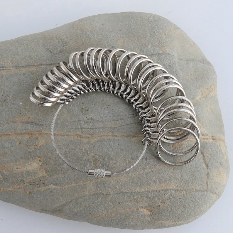 May include: A silver ring sizer with a chain and a clasp. The sizer has a series of rings of different sizes.