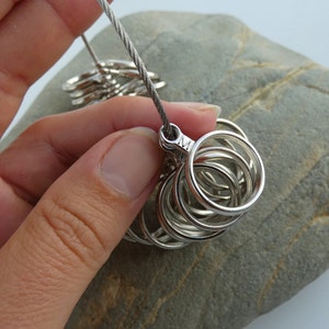 May include: A set of silver ring sizers with a metal cable attached. The sizers are stacked in a circle and the cable is looped through the top ring.