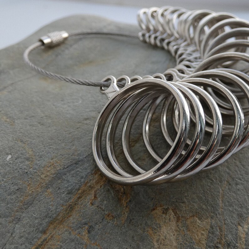 May include: A silver ring sizer with a chain and a clasp. The sizer has a series of rings of different sizes.