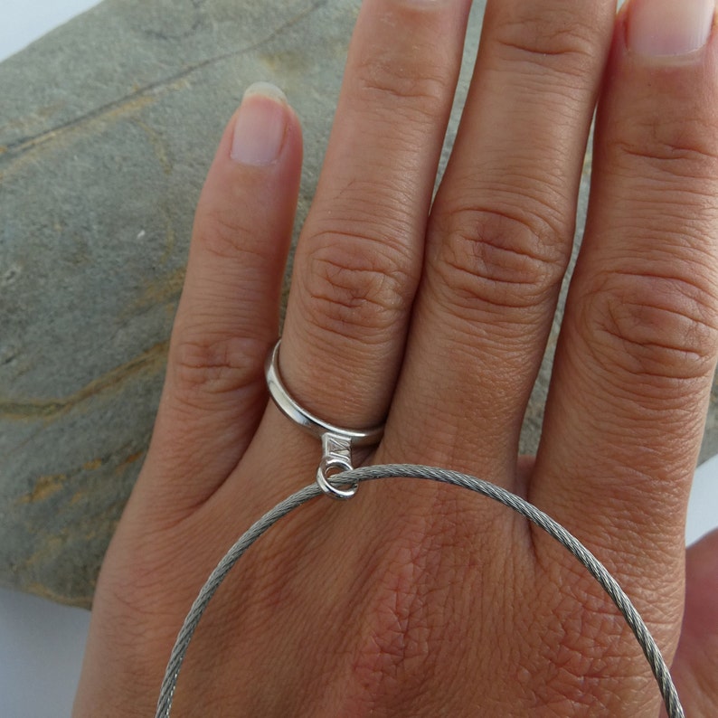 May include: A silver ring with a small loop attached to a silver cable chain bracelet.