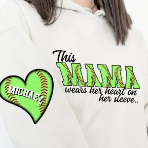 May include: A cream-colored hoodie with a green heart-shaped baseball design on the left sleeve, personalized with the name "MICHAEL". The text "This NANA wears her heart on her sleeve.." is printed on the front.