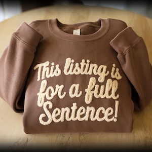 May include: A brown crewneck sweatshirt featuring the cream-colored, textured, embroidered text "This listing is for a full Sentence!" across the chest. The garment has long sleeves, a ribbed collar, and a soft, fleece-lined interior fabric.