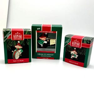 May include: Three Hallmark Keepsake Christmas ornaments from the Collector's Series. Each ornament features a small elf in a green and red outfit. The boxes are green with red accents and the text "Hark! It's Herald".