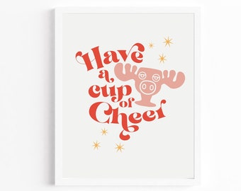 Pode incluir: Uma impressão emoldurada branca com uma ilustração vermelha e rosa de um alce com o texto "Have a cup of Cheer" em letras vermelhas e brancas.