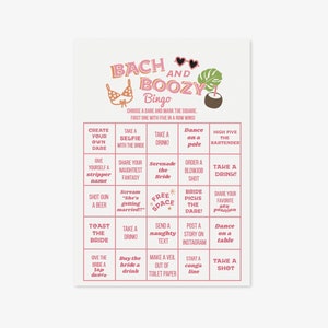 May include: A pink and white "Bach and Boozy Bingo" game card. The card features a bikini, sunglasses, and tropical leaf graphic. The bingo card has various dares such as "Take a drink!" and "Dance on a table."