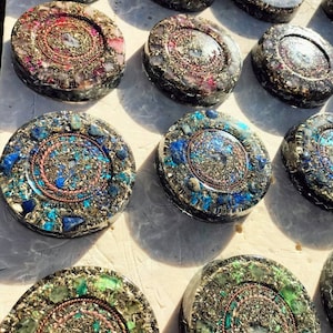 Könnte beinhalten: Eine Sammlung von 10 runden, flachen, kristallinfundierten Untersetzern mit einem Kupferdrahtmuster. Jeder Untersetzer zeigt eine andere Kombination aus Kristallen und Farben, darunter Blau, Grün, Lila und Pink.