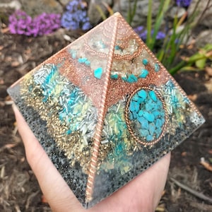 May include: A handcrafted pyramid with a copper wire frame and embedded turquoise stones. The pyramid features layers of gold, silver, and turquoise accents, creating a unique and decorative piece. The base is approximately 7.6 cm square.