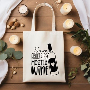 Könnte beinhalten: Weiße Stofftasche mit schwarzem Text und einer Weinflaschengrafik. Der Text lautet "Some Groceries Mostly Wine" mit einem Herzen auf der Weinflasche.