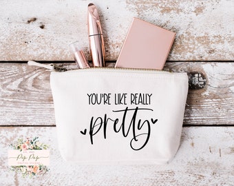 May include: White canvas zippered pouch with the text "You're like really pretty" in black lettering. The pouch is partially open and contains a rose gold compact mirror, a rose gold mascara tube, and a clear lip gloss tube.